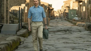 Pompeii: Out of Time with Tom Hiddleston TV show screenshot 1: Hiddleston walking on an ancient stone street at sunset, carrying a bag.