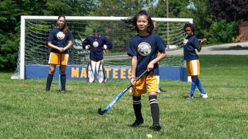 Popularity Papers TV show screenshot 3: Julie stands in front of the field hockey team with her stick in hands and a smile on her face.