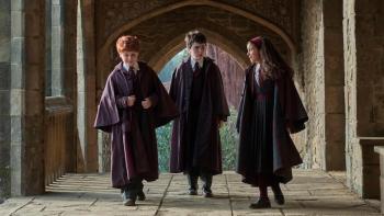 Harry Potter and the Philosopher's Stone screenshot: Ron, Harry, and Hermione walk on the Hogwarts campus in their robes