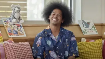 Reading Rainbow TV show screenshot 1: Host Mychal the Librarian smiles broadly at the camera in a cozy space surrounded by books.