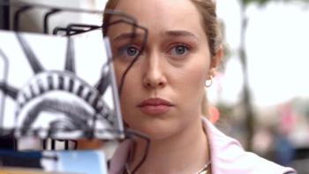 Saint X TV show: Emily stands next to a rack of New York City postcards staring at something off-screen. Her face, shown in closeup, appears sad and frightened. 