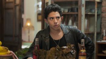 Sergio Palau wears a black leather coat, a black tank top, and a necklace. He leans his arm on a table.