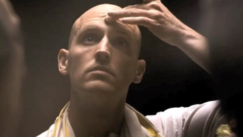 Krishnas: Gurus. Karma. Murders TV show screenshot: A bald white man in monk robes puts his hand to the middle of his forehead.