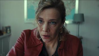 A blonde women in an all-crimson outfit looking intensely ahead at someone else