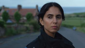 The Red King TV show screenshot: A dark-haired Brown woman look solemnly at something with a wintry coastal background