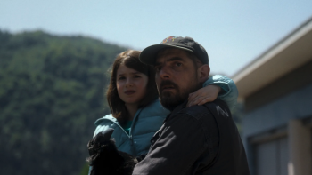 The Hunt TV show screenshot: A tense man holds a young girl protectively outside a rural home, both looking off-screen with concern