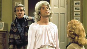 Soap: Jodie is center-screen, wearing a blonde wig and a pink dress; Burt stands behind him, looking disgusted, Mary's head is seen from behind