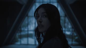 Camila Morrone. She has blood coming out of her nose. She stands in front of a large triangular window.