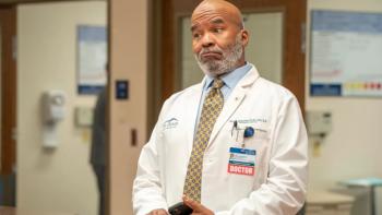 St. Denis Medical TV show screenshot 1: Dressed in a doctor's white coat, Ron stands in a hospital corridor looking unpleasantly surprised