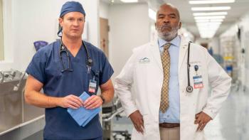St. Denis Medical TV show screenshot 2: Bruce and Ron stand in a hospital corridor in scrubs and a white coat respectively, confronting a problem