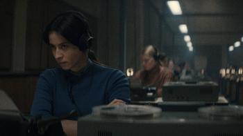 Agnes O’Casey sits at a desk in front of a recorder. She wears over ear headphones and a blue sweater.