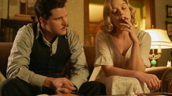 Strange Angel TV Series: A man and a woman in 1930s-period clothes sit together on a couch, talking; she is smoking a cigarette. 