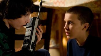 Stranger Things TV show screenshot 1: Mike and Eleven face each other in Mike's basement while Mike holds a walkie-talkie