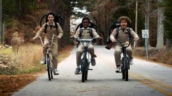 Stranger Things Season 2 TV show screenshot 1: Mike, Dustin and Lucas ride bikes while wearing Ghostbuster costumes