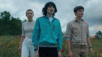 Stranger Things Season 5 TV show screenshot 1: Eleven, Mike and Noah stand on a grassy field with flowers and the blue sky behind them