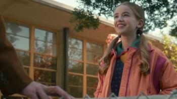 Stranger Things Season 5 screenshot 3: Holly smiles at a person off-camera; we see the hand of a young man in a brown suit from a person off-camera