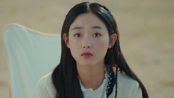 Lee Yoo-mi as Nam-soon sits on a white chair in front of a blurry field. She stares into the distance.