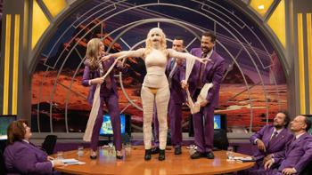 Superstar TV show screenshot 2: Loly stands on the desk on a Spanish TV show, wrapped in bandages, with the show hosts and helpers surrounding her