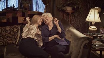 Tales of the City TV: Mary Ann and Anna snuggle close together on a Victorian couch, smiling while holding cigarettes