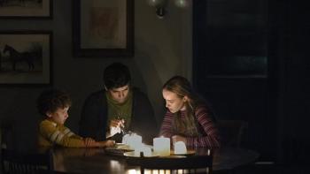 Teacup screenshot 2: Arlo, Nicholas, and Maryl sit around a dining room table, lit by several candles. They're peering at something with a flashlight.