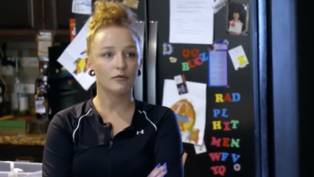 Teen Mom: The Next Chapter TV show screenshot 1: Maci wears red hair in bun and stands in kitchen with black shirt and arms crossed. 
