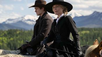 The Abandons TV show screenshot 2: Lucas Till and Gillian Anderson ride horses. They wear dark hats and dark overcoats. Mountains in the background.