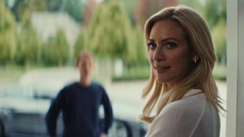 Brittany Snow looks over her shoulder while standing in a doorway. She wears a white sweater.