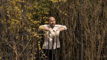 The Crowded Room: Lior Raz stands in an overgrown field, leaning on a wrought iron fence. 