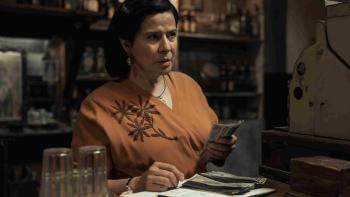 The Dead Girls TV show screenshot 2: Arcelia Ramírez holds money at a register. She wears a dark orange blouse with a brown floral on one side.