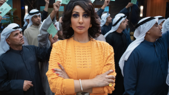 The Exchange TV show: Munira stands in front of Kuwaiti traders on the floor staring at camera with arms crossed. 