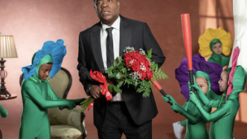 The Fall and Rise of Reggie Jenkins screenshot 1: Reggie Dinkins holding flowers while children in flower costumes hit him with props. 