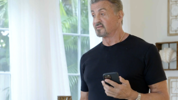 The Family Stallone screenshot 1: Sylvester Stallone talks into his cellphone wearing black t-shirt. 