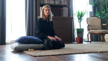 The First TV Series: Laz (Natasha McElhone) sits yoga-style on a beige rug in an upscale living room.