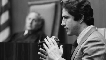 The Hillside Strangler screenshot 3: Black and white image of Kenneth Bianchi talking on witness stand with judge watching.