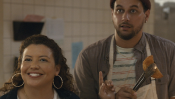 The Horror of Dolores Roach screenshot 1: Justina Machado as Dolores and Alejandro Hernandez as Luis stand in kitchen with empanada.