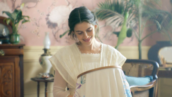 The House of the Spirits screenshot 1: Rosa smiling while embroidering in a vintage room with soft pink decor.