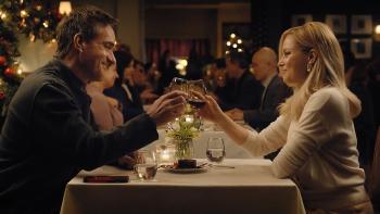 The Miniature Wife TV show screenshot 2: MacFadyen and Banks toast a glass of wine. MacFayden wears a dark shirt, Banks wears a white shirt.