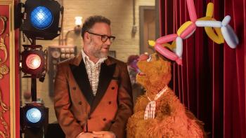 The Muppet Show 2026 TV show screenshot 4: Fozzie Bear, wearing a balloon hat, talks to Seth Rogen backstage