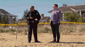 Michael Beach in police uniform and Tim Bagley in a suit jacket stand at an active crime scene on the beach.