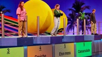The Quiz with Balls TV show screenshot: Three people stand at the end of ramps with the middle person on the verge of being hit by a huge ball.