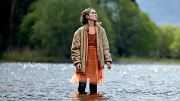 The Rising TV show screenshot 1: A 19-year-old girl stands in the middle of a lake wearing a dress and a coat.