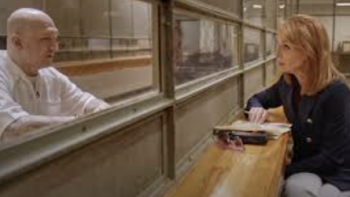 The Takedown: American Aryans TV show screenshot 2: Brown haired reporter talks through prison glass to former bald ABT member in white. 