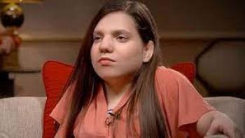 The Curious Case of Natalia Grace TV show screenshot: A closeup shot of a woman with dwarfism is shown as she sits unsmiling on a coach.