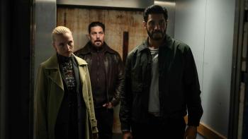 The Asset TV show screenshot 3: A petit blonde women in a green overcoat and two muscular men in leather jackets with dark hair stand in an elevator
