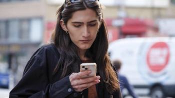 A woman with long brown hair looks down at her phone, her sunglasses pushed up on her head.