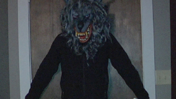 The Creep Tapes screenshot 2: A man in a black sweatshirt and werewolf masks stands with his back and arms against a wooden door