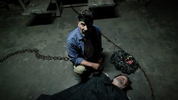The Creep Tapes screenshot 3: A man kneels on an industrial-looking floor next to an unconscious man flat on his back. Heavy chains lay on the floor 