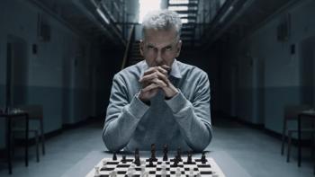 The Devil's Hour TV show screenshot 4: A man in a grey shirt is pictured sitting at a table with a chessboard in front of him. His hands are clasped a