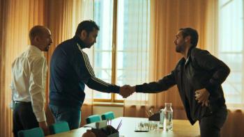 Helicopter Heist TV show screenshot 1: Two men in casual wear shake hands over a table while a third man in a white button up shirt looks on