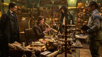 The Librarians The Next Chapter TV: In a warm-lit study room, Vikram, Charlie and Connor look to Lyra who sits with a telescope in a busy office desk.